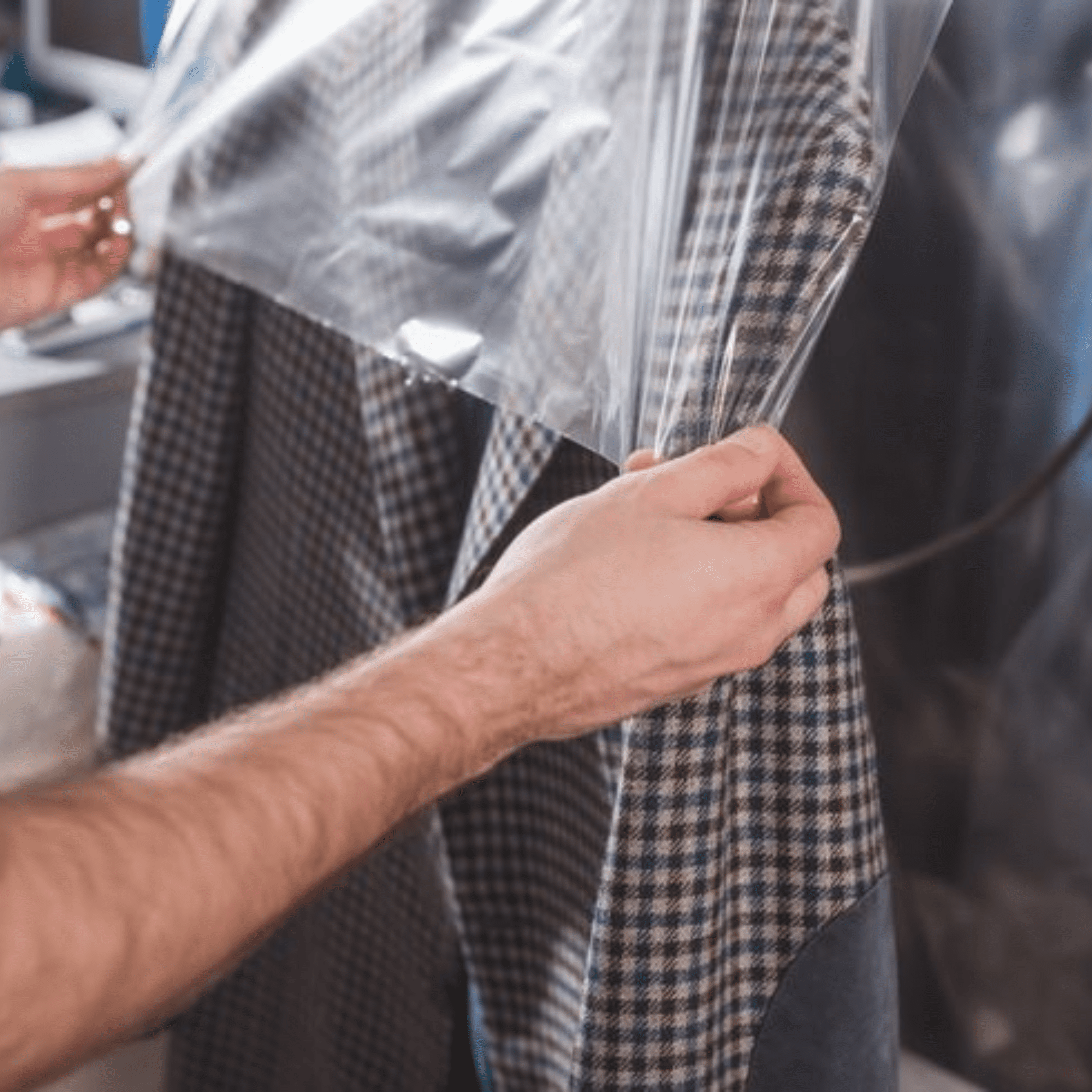 Person covers a plaid jacket with clear plastic garment bag, likely for storage or after dry cleaning.