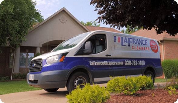A LaFrance Cleaners delivery van is parked in the driveway of a suburban house on a sunny day.