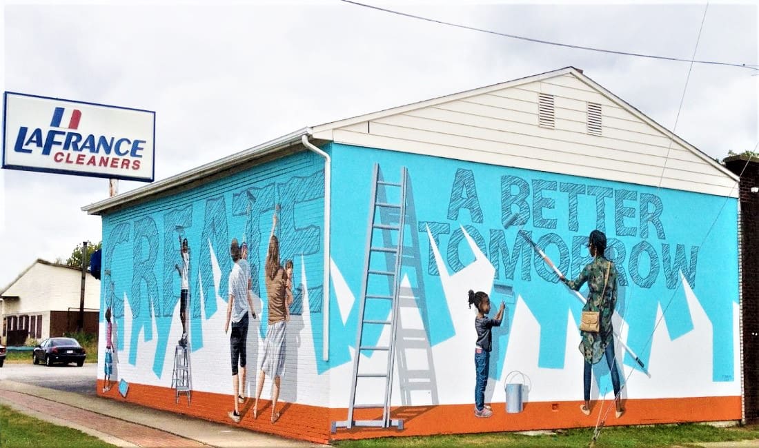 A mural on a building shows people painting the words "CREATE A BETTER TOMORROW." A LaFrance Cleaners sign is visible on the roof.