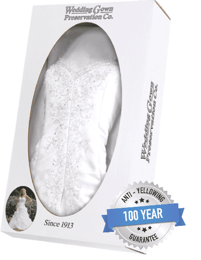 A white wedding dress is displayed in a preservation box labeled "Wedding Gown Preservation Co." with a "100 Year Anti-Yellowing Guarantee" badge and "Since 1913.