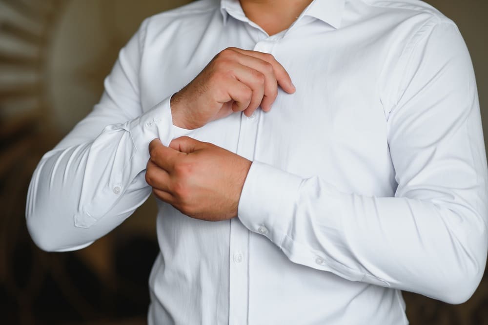 A person in a white dress shirt fastens the cuff of their sleeve with one hand.