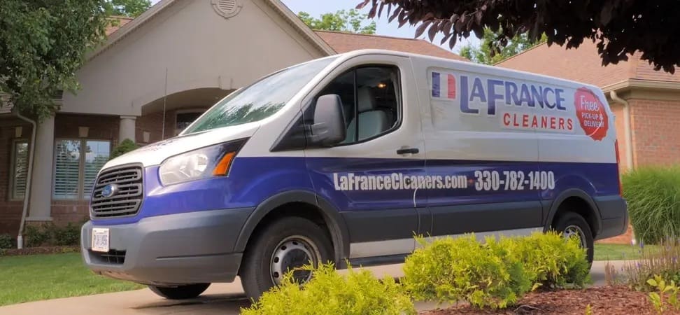 A LaFrance Cleaners van is parked in the driveway of a suburban house, displaying the company’s logo and contact information on its side.