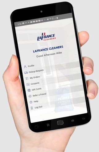 A hand holds a smartphone displaying the LaFrance Cleaners app home screen with menu options including Profile, Pickup Request, My Orders, and more.