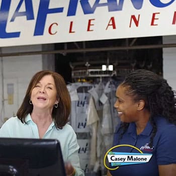 Two women stand behind a counter at a dry cleaners called LaFrance; one is wearing a uniform, and a caption reads "Casey Malone.